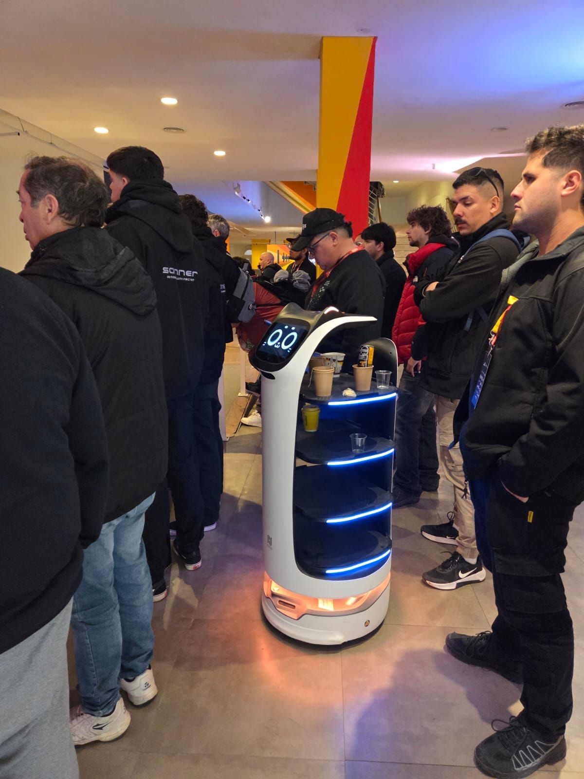 Asistentes rodeando al robot de servicio del evento en el hall del Borges